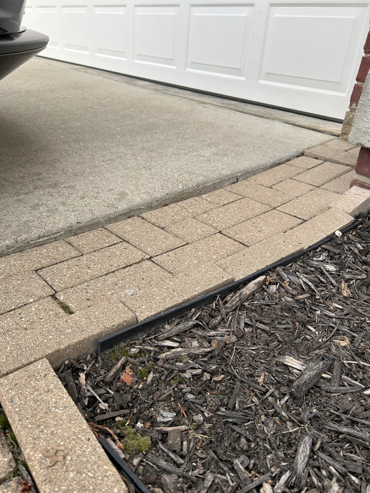 Patio edge with failed restraint and pavers shifting toward the mulch bed